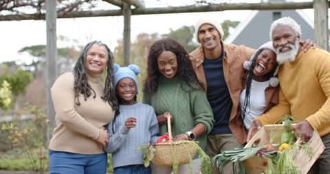Multigenerational Black family harvesting vegetables in backyard garden under pergola