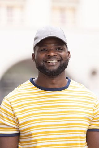 Smiling african man wearing grey cap and yellow striped t-shirt in sunlit urban courtyard
