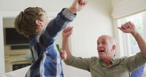 Joyful Grandfather and Grandson Raising Hands at Home