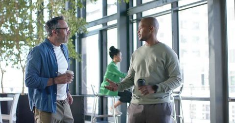Colleagues chatting in coworking lounge with coffee, casual business conversation