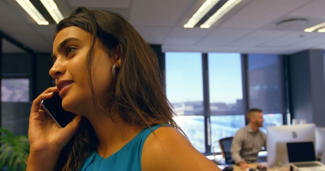 Businesswoman Talking on Phone at Modern Office with Colleague in Background - Download Free Stock Images Pikwizard.com