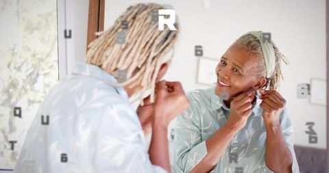 Senior woman fastening earrings at mirror smiling in natural light home portrait