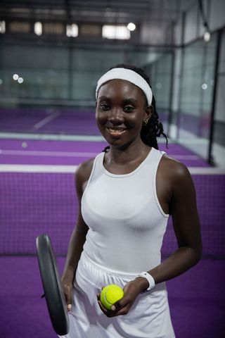 African american tennis player standing on purple court smiling in white athletic outfit