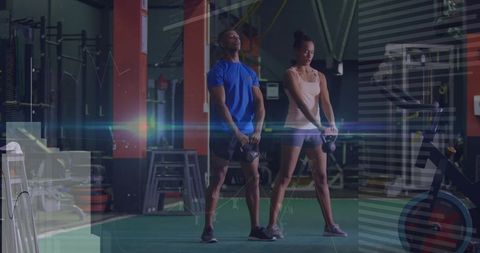 Two Partners Lifting Kettlebells on Turf in Industrial Gym for Strength and Conditioning