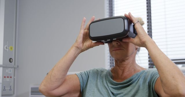 Senior woman wearing VR headset, taking part in immersive experience indoors. Use to illustrate technology adoption among older adults, advancements in virtual reality, and innovation in elderly care.