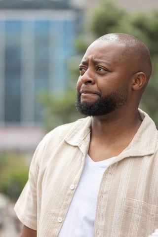 Contemplative african man gazing right in urban plaza wearing beige shirt and white tee