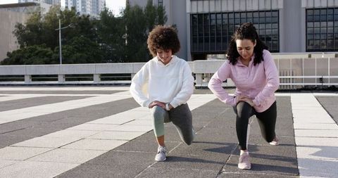 Women lunging on rooftop terrace urban outdoor fitness workout duo in activewear