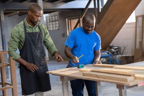 African american carpenters measuring wood for custom furniture workshop collaboration