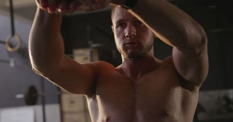 Shirtless athlete engaging in intense kettlebell workout in gym