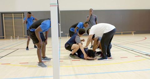 Volleyball teammates supporting injured player on indoor court during training session