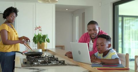 African american family cooking with parents helping child using laptop on kitchen island