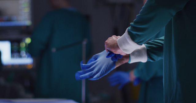 Surgeon wearing gloves in a dimly lit operating room. Ideal for use in healthcare articles, hospital brochures, surgical procedure explanations, or medical training materials. Shows careful preparation and adherence to hygiene standards.