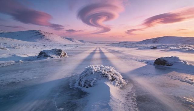 Frost-covered shrub on frozen river at sunrise with swirling spiral cloud vortex, alpenglow