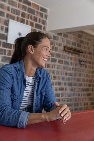Smiling woman leaning on red countertop in rustic brick kitchen