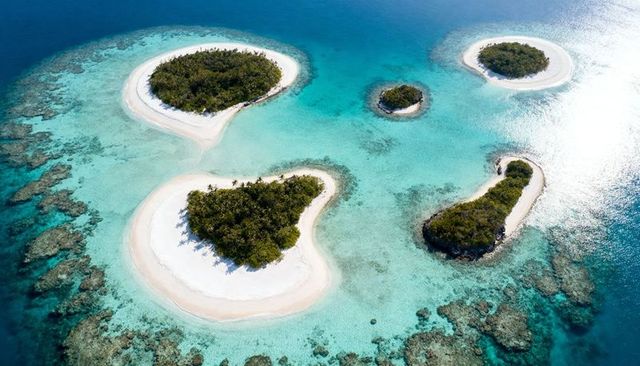 Aerial panorama of five tropical islets in turquoise lagoon with white sand and reefs