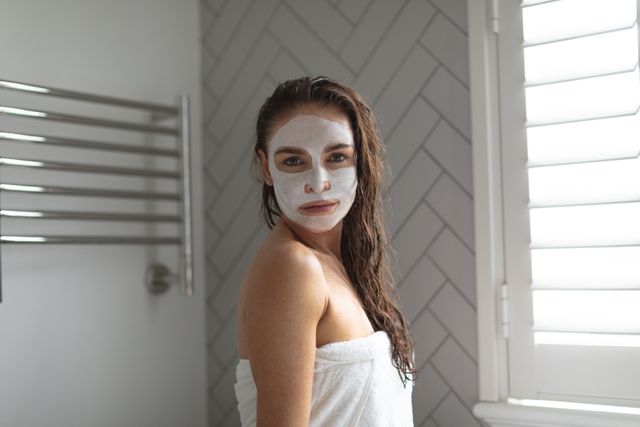 Portrait of woman with facial mask standing in bathroom at home