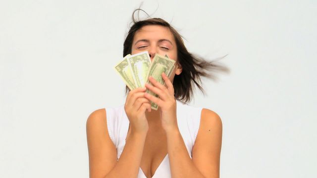 Young woman holding cash joyfully with wind blowing hair, conveying a sense of financial happiness and success. White background enhances focus on subject, making this useful for finance, banking, or investment themes.