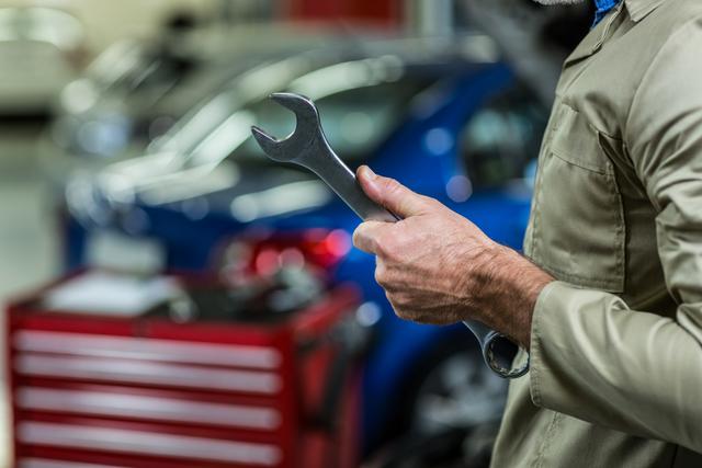 Mid-section of mechanic holding wrench tool in repair garage