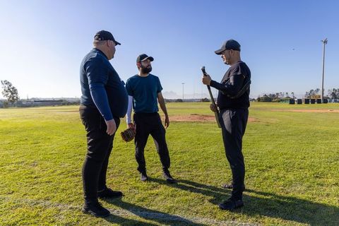 Baseball coaches and player discussing bat technique on grassy sunny practice field
