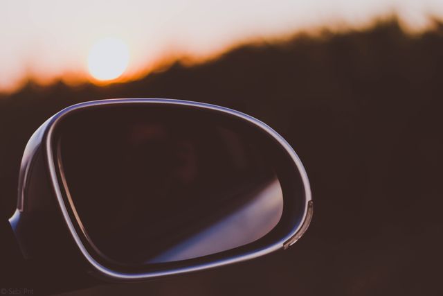 Side mirror of a car reflecting bright sunset sky. Great for themes of travel, evening journeys, peaceful drives, transportation, and the beauty of nature at dusk. Perfect for use in automotive advertising, travel blogs, and any media promoting the allure of road trips during twilight hours.