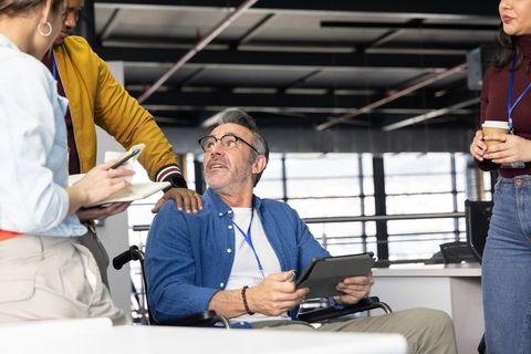Senior professional in wheelchair collaborating with diverse team in modern office