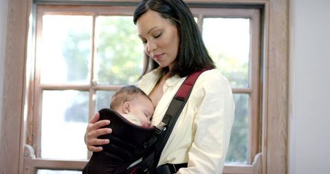 Mother embracing newborn in infant carrier by sunlit window