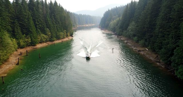 A boat cuts through the tranquil waters of a forest-lined lake, leaving a V-shaped wake behind, with copy space. This aerial view captures the serene beauty of a natural landscape and the leisure activity of boating.