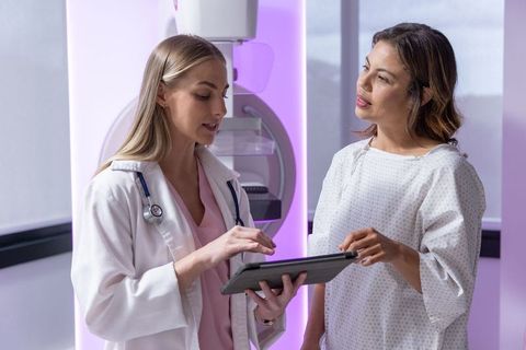 Female clinician consulting with gowned patient at mammography appointment using tablet