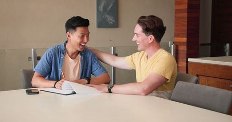 Asian Man Writing, Friend Encouraging During Study Session
