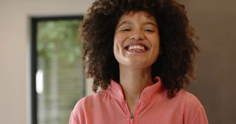 Smiling woman in pink zip-up textured top with curly hair, warm natural-light portrait