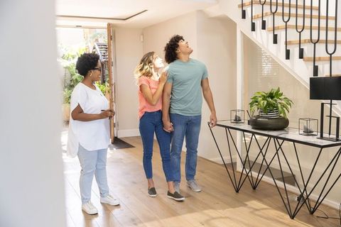 Young diverse couple touring new home with realtor holding keys and admiring staircase and entryway