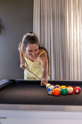 Smiling young woman aiming pool cue on black-felt table with racked colorful billiard balls