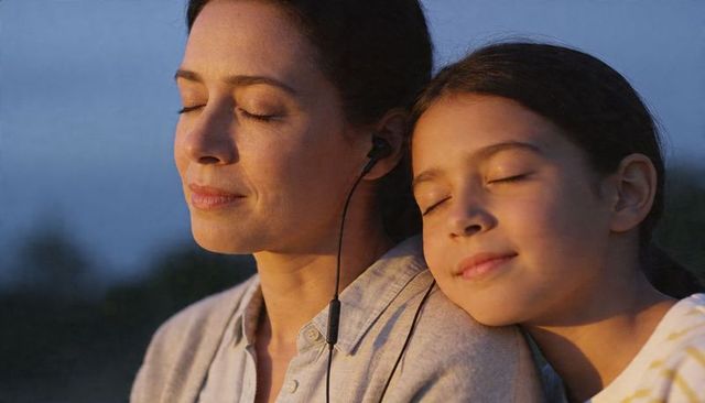 Mother and daughter sharing wired earbuds at sunset relaxing and bonding outdoors