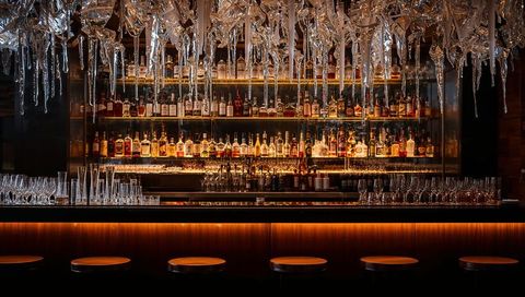 Luxury bar with backlit liquor shelves and crystal chandelier glowing over wood counter