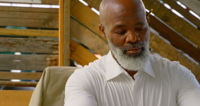 African American man in a white shirt sits thoughtfully, with copy space. He appears to be in a contemplative mood in a rustic outdoor setting.
