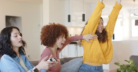 Multicultural friends celebrating gaming victory on couch in cozy open-plan living room
