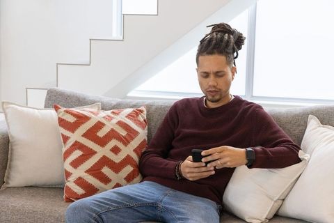African american man relaxing on sofa using smartphone in modern minimal living room
