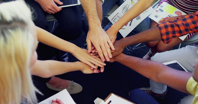 Group of diverse individuals placing hands together in a show of unity and teamwork. Ideal for use in business content, diversity and inclusion initiatives, team building activities, collaborative projects, and promoting workplace solidarity and support.