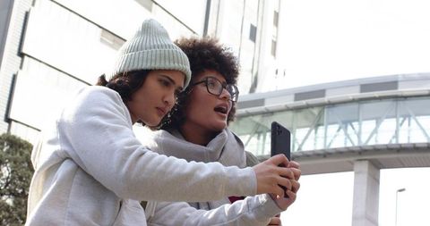 Friends taking selfie near modern skybridge wearing winter beanies and casual hoodies
