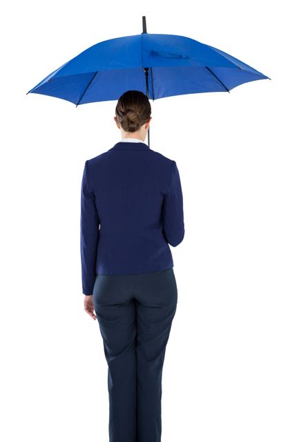 Businesswoman in formal attire holding a blue umbrella, viewed from the back against a white background. Ideal for use in corporate presentations, business-related articles, and advertisements focusing on professional attire, weather protection, and corporate themes.
