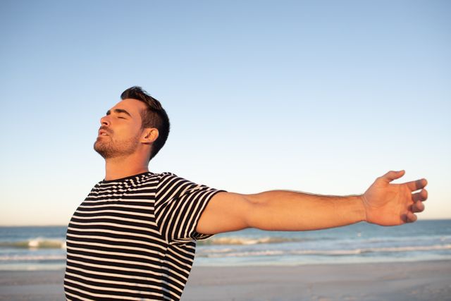 Man standing on beach with arms outstretched, enjoying the freedom and tranquility of the ocean. Ideal for concepts of relaxation, freedom, nature, and peacefulness. Suitable for travel promotions, wellness blogs, and lifestyle advertisements.