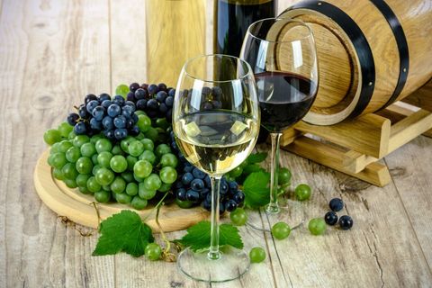 Serving red and white wine with fresh grapes and oak barrel on rustic wooden table