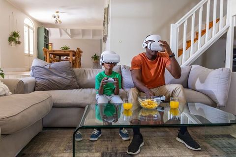 Father and Son Playing VR Games on Sofa, Sharing Snack and Bonding in Bright Modern Home