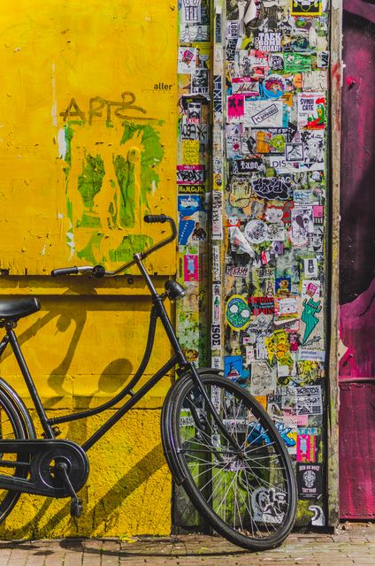 Bicycle leaning against an exterior wall creatively decorated with numerous colorful stickers and graffiti. Ideal for illustrating urban street culture, transportation methods in cities, alternative lifestyles, and creative urban spaces or backgrounds for artistic projects.