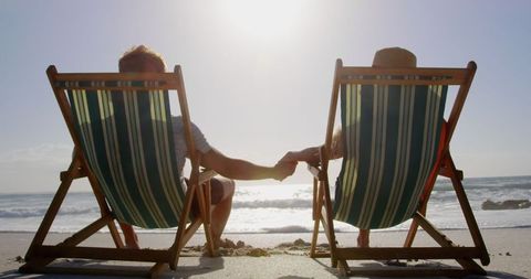 Couple Relaxing on Beach Loungers Holding Hands at Sunset