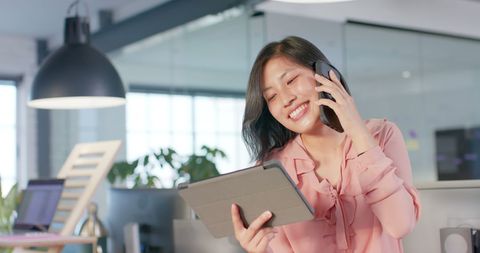 Happy Businesswoman Multitasking with Tablet and Phone in Office