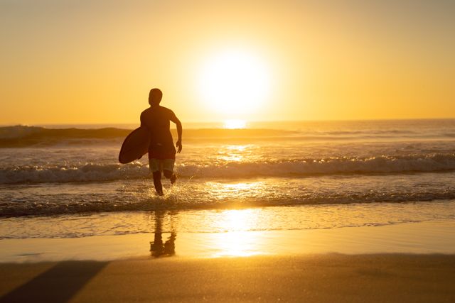 Man running with surfboard on the beach during sunset