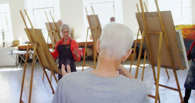 Senior individuals participating in an art class, engaging in a thoughtful discussion. Ideal for illustrating concepts related to senior education, creative activities for the elderly, and community workshops. This image can be used in articles about elderly engagement in creative projects, promotion of art classes for seniors, and educational program brochures.