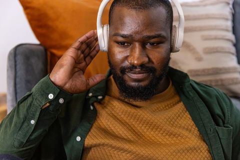 African american man adjusting wireless headphones while enjoying music on cozy sofa