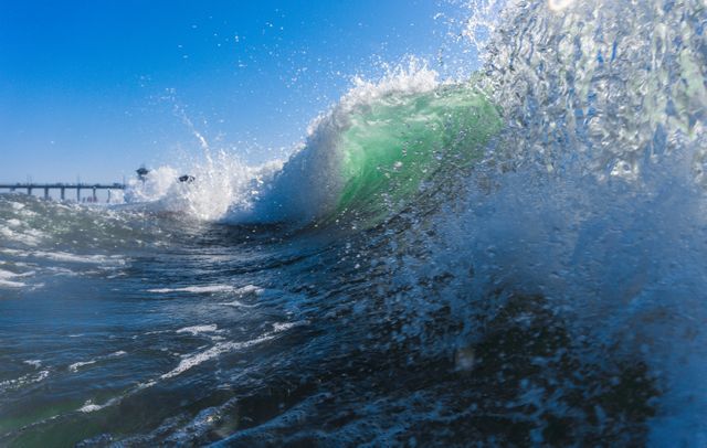 Dynamic image capturing an ocean wave mid-crash under a bright blue sky, creating a beautiful spray of water droplets. Great for themes related to nature, marine life, summer vacations, surfing adventures, water sports, coastal environments and sea-related activities.